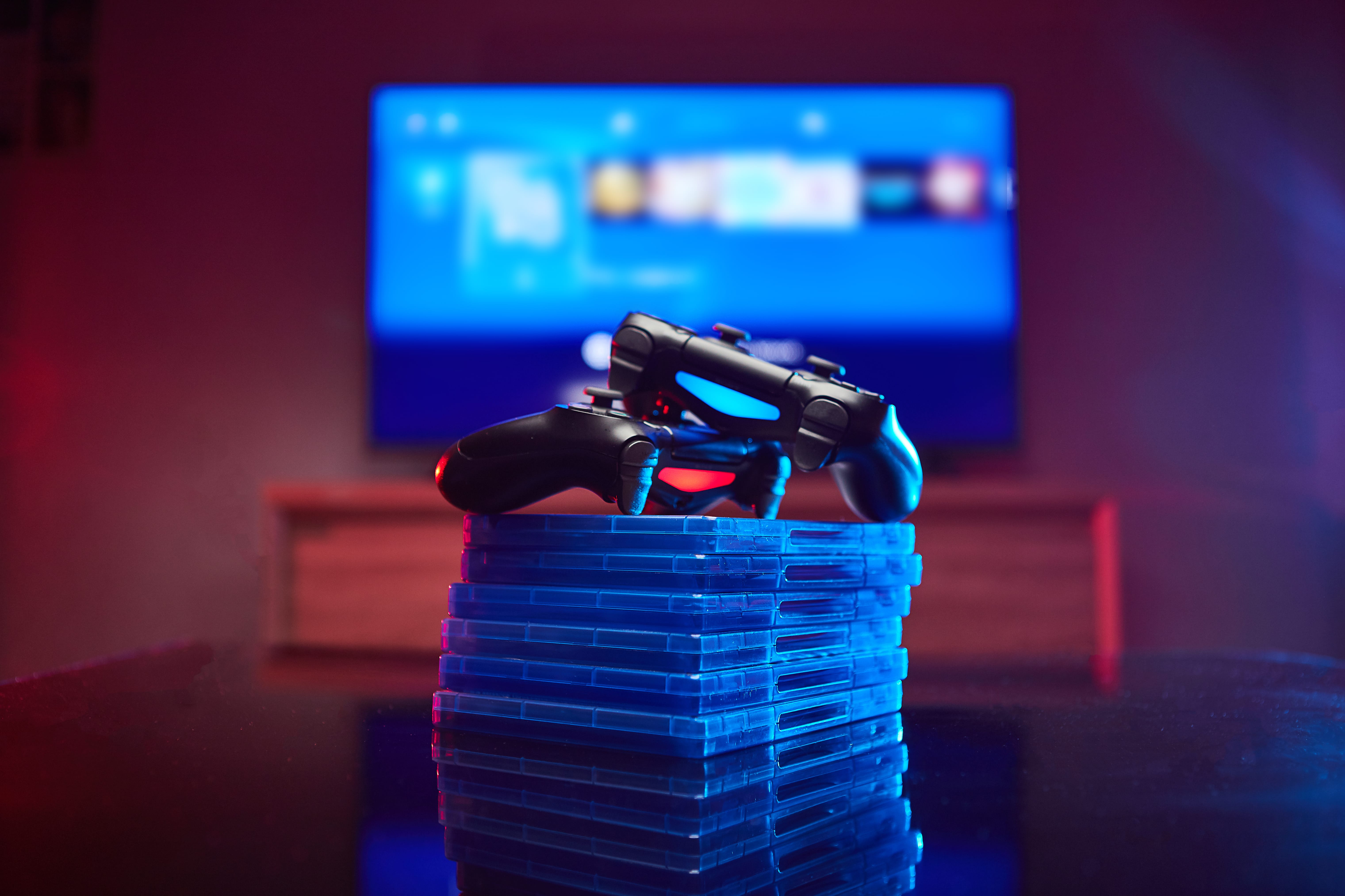 PS4 Dualshock 4 controllers on stack of games, Blurred TV in background
