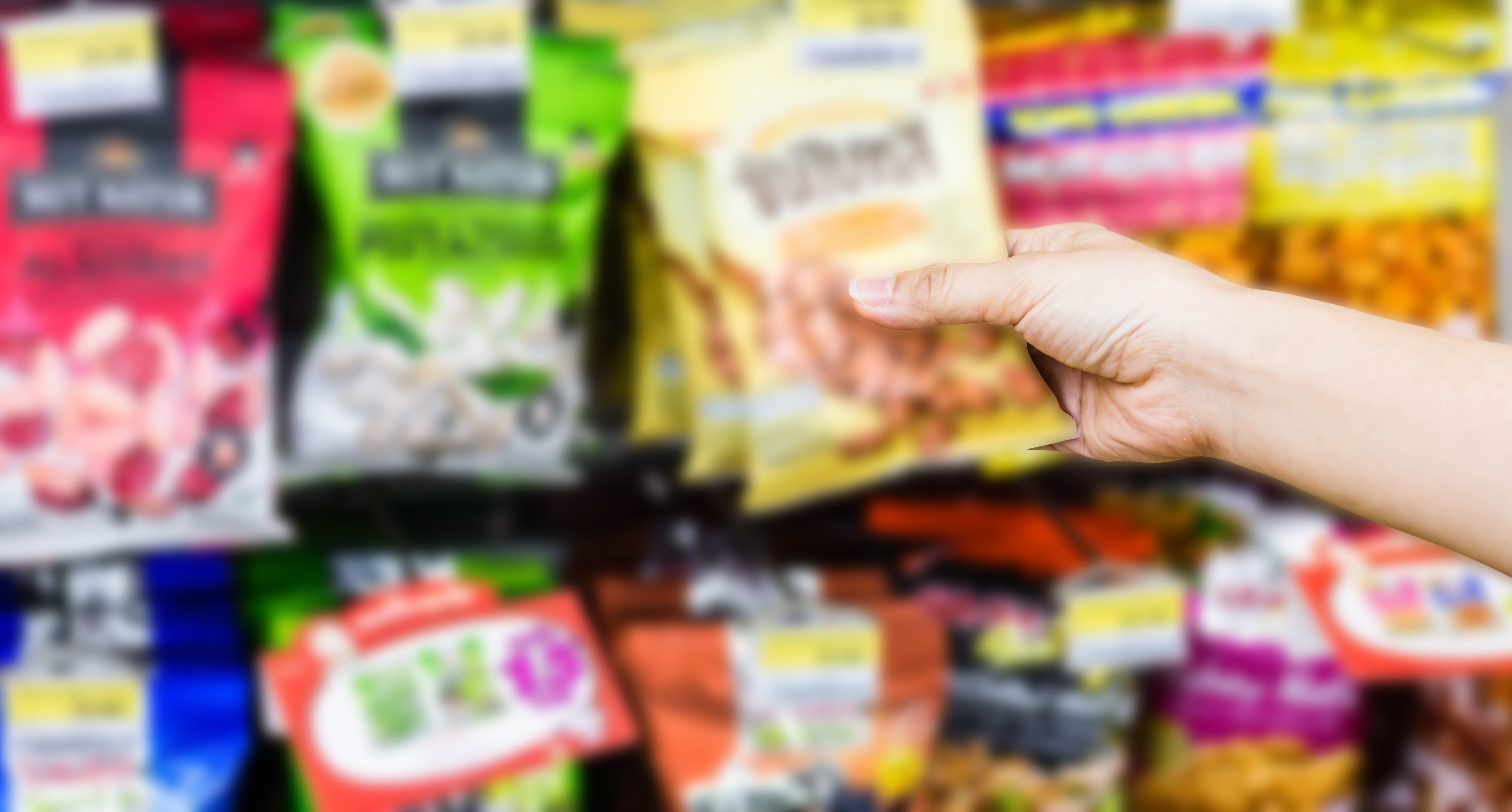 Hand grabbing a bag of snacks from a rack with many options